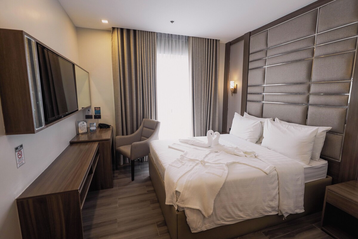 Ein Hotelzimmer mit Bett, Schreibtisch, Stuhl, Fernseher und einem großen Fenster mit Vorhängen.
