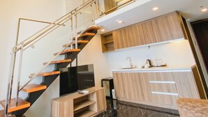 A modern kitchen with a built-in island, a staircase with glass railings, and a flat-screen TV. - El Vistra Hotel (Angeles City)