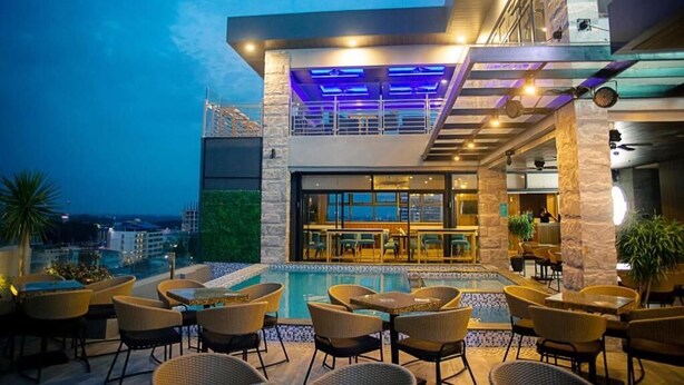 A rooftop bar with outdoor seating, a pool, and a view of the cityscape. - El Vistra Hotel (Angeles City)