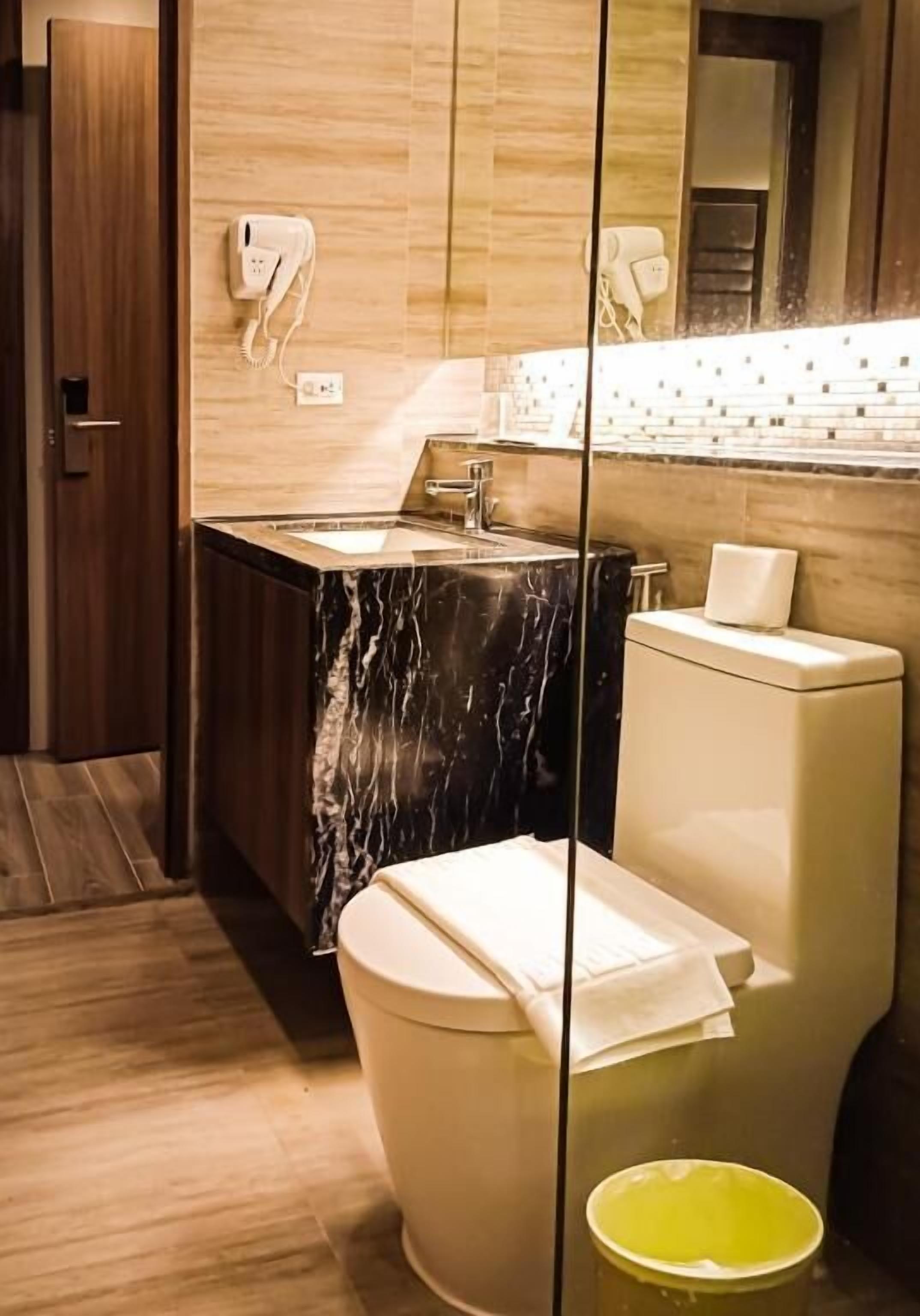 Une salle de bain avec un lavabo en marbre, des toilettes, un miroir et un seau jaune.