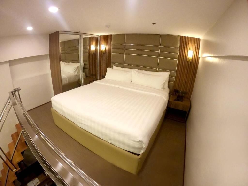 Une chambre d’hôtel moderne dotée d’un grand lit, d’une douche à parois de verre et d’une tête de lit incurvée.