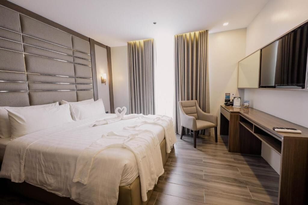 Ein Hotelzimmer mit einem großen Bett, einem Schreibtisch, einem Sessel und einem Fernseher.