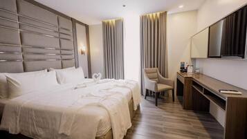 Ein Hotelzimmer mit einem großen Bett, einem Schreibtisch, einem Sessel und einem Fernseher.