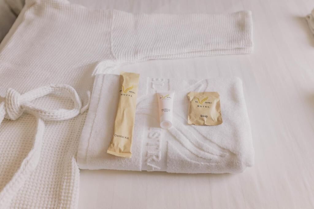 Een keurig gevouwen witte handdoek met toiletartikelen, waaronder een tandverzorgingsset, een zeepstuk en een tube lotion.