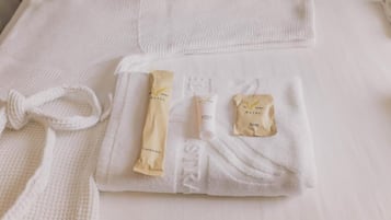 Toalha branca dobrada com produtos de higiene, incluindo kit dental, sabonete em barra e um tubo de loção.