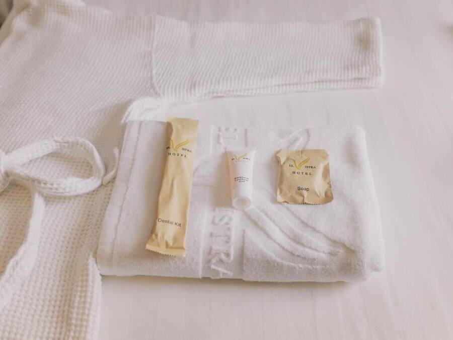 Toalha branca dobrada com produtos de higiene, incluindo kit dental, sabonete em barra e um tubo de loção.