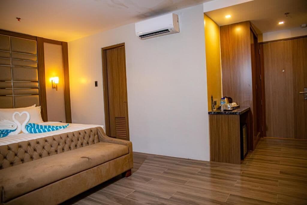 A hotel room with a bed, a small kitchenette, a wardrobe, and an air conditioning unit.