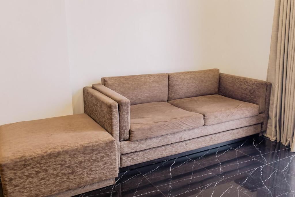 A room with a sofa and a matching ottoman, a dark tiled floor, and a curtain on the right.