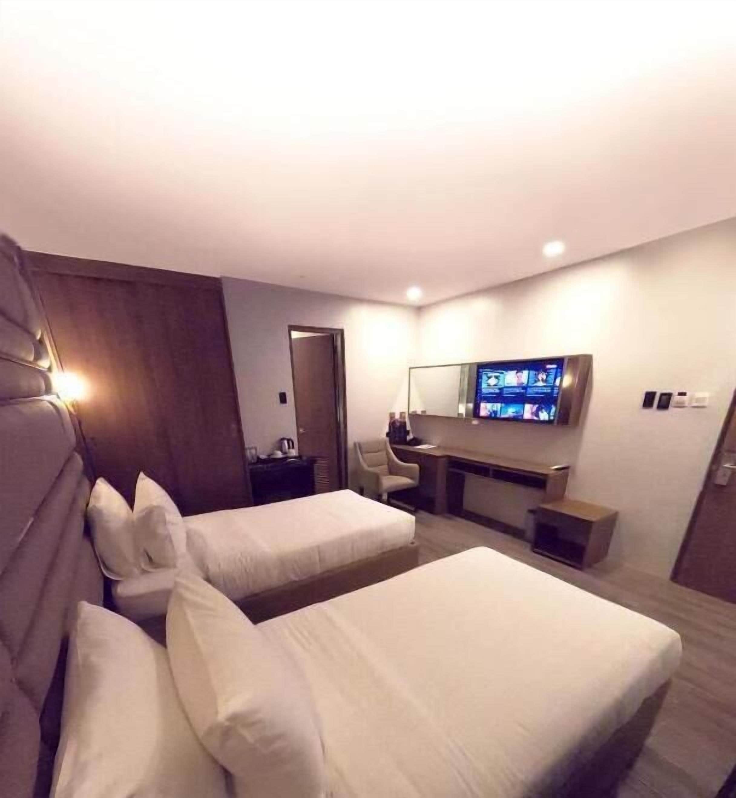 Habitación de hotel con dos camas, un escritorio, un televisor y un espejo.