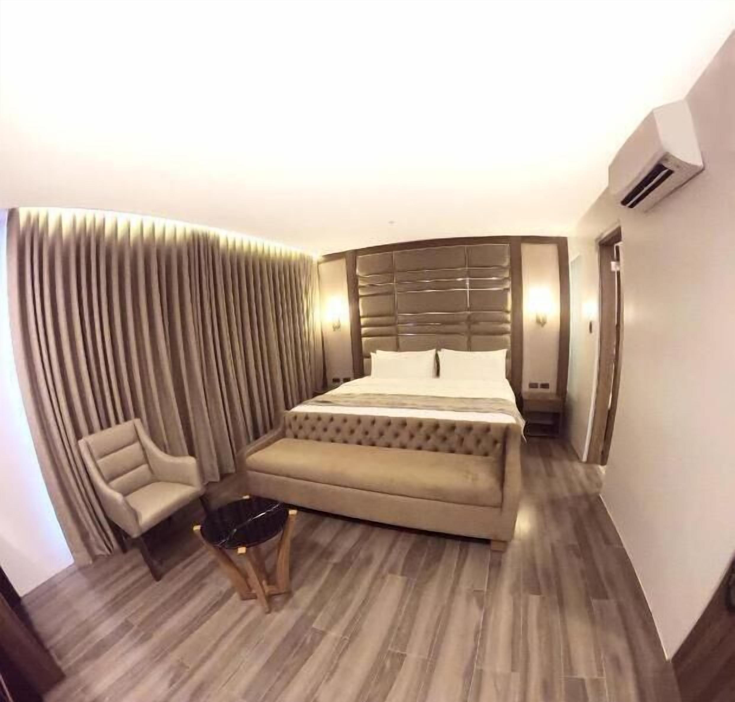 A hotel room with a bed, a chair, a small table, and a wall-mounted air conditioner.