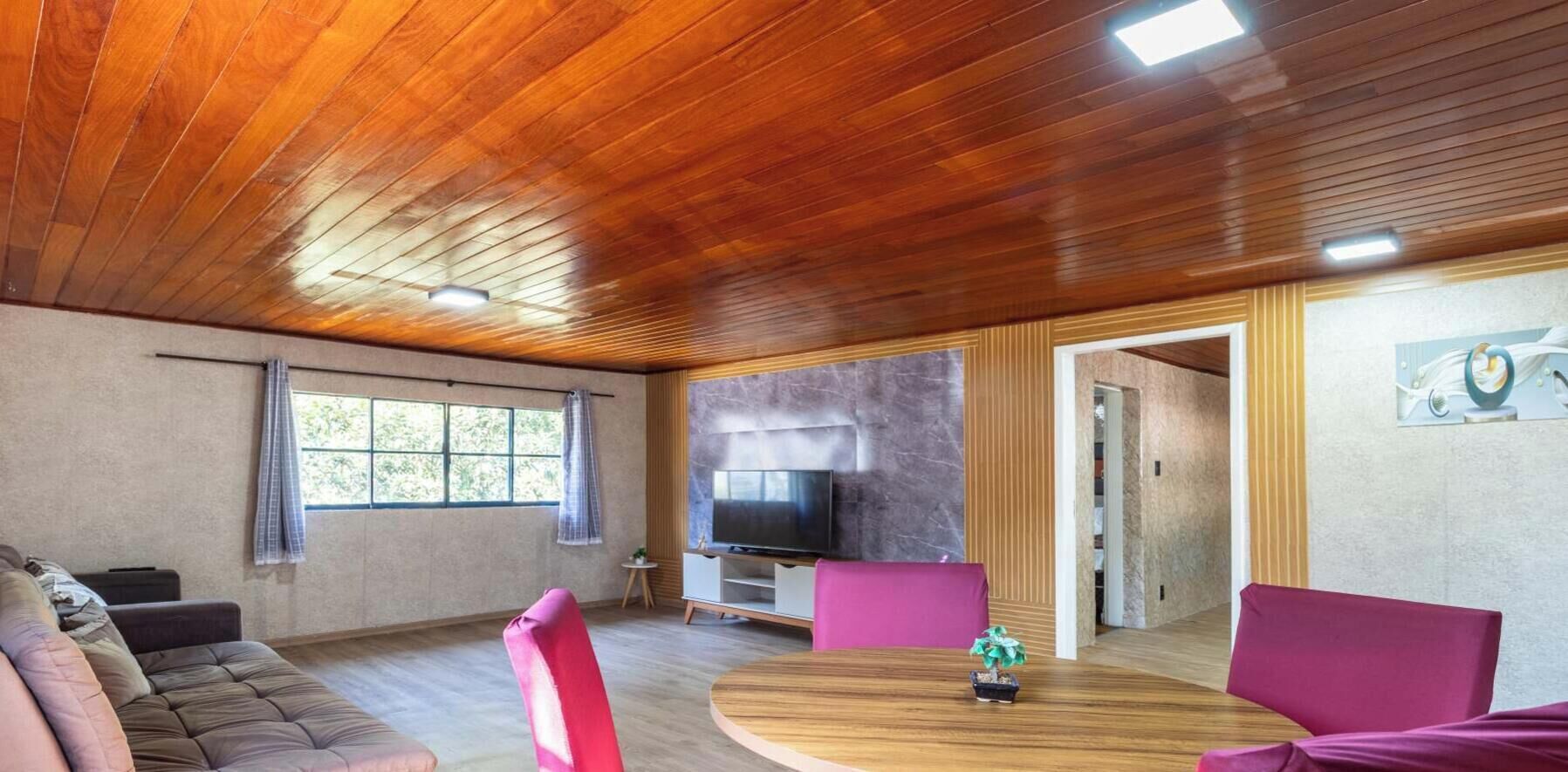 Een moderne woonkamer met een houten plafond, een televisie, een ronde houten tafel en een bank.
