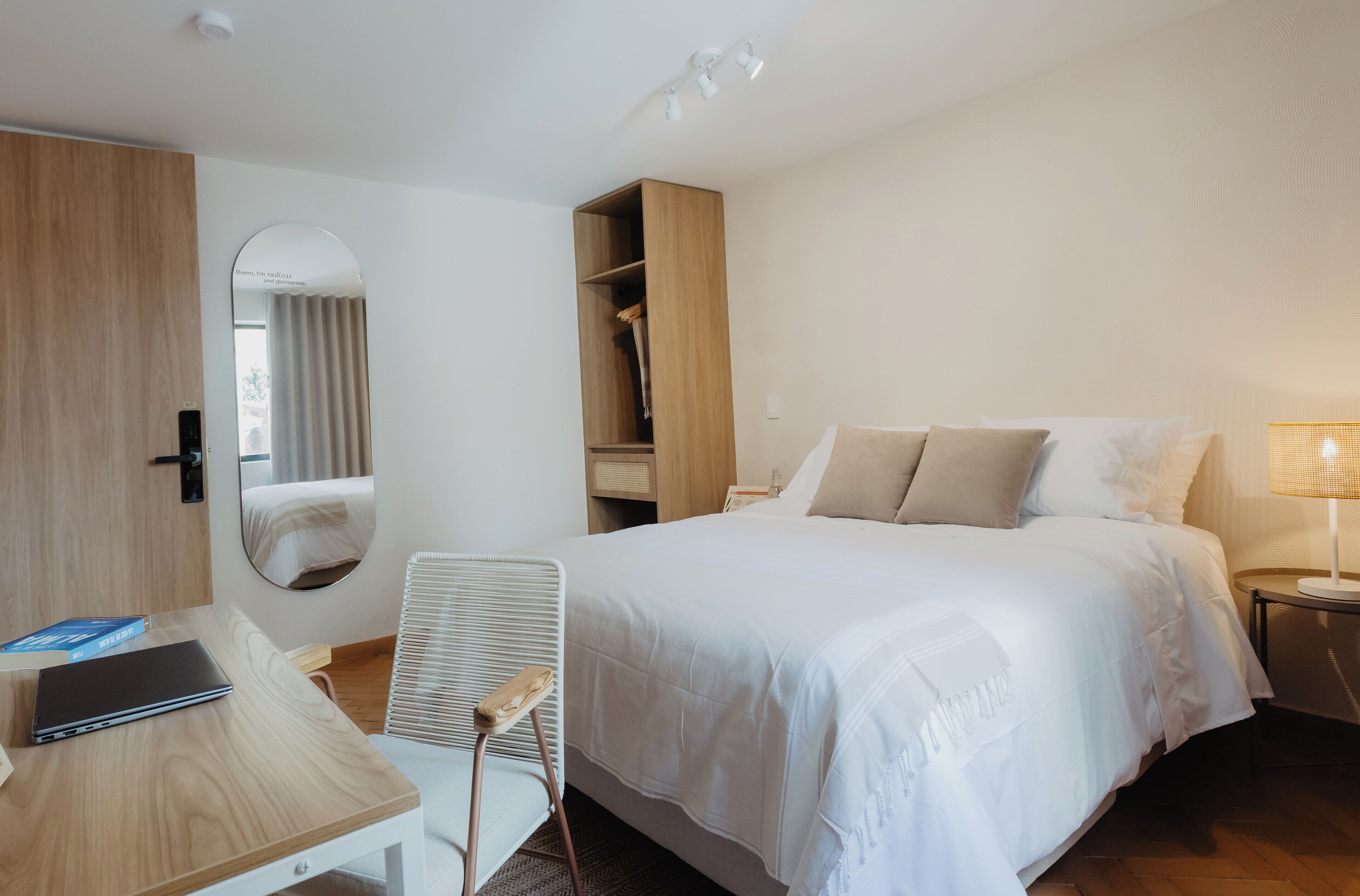 A hotel room with a bed, a desk, a chair, a wardrobe, and a mirror.