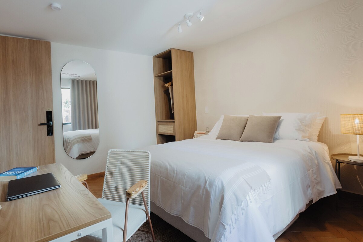 A hotel room with a bed, a desk, a chair, a wardrobe, and a mirror.