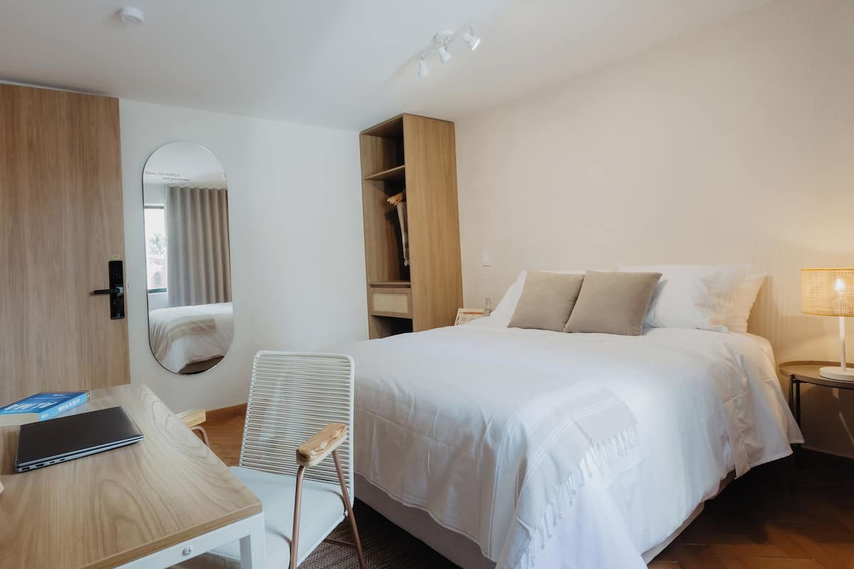 Hotellihuone, jossa on sänky, työpöytä, tuoli, vaatekaappi ja peili.
