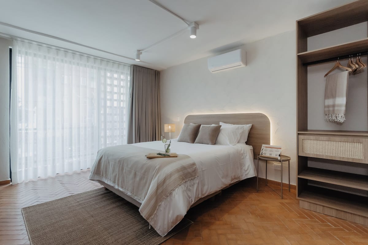 Moderni hotellihuone, jossa on suuri sänky, yöpöytä lampun kanssa, pieni sivupöytä ja sisäänrakennettu vaatekaappi, jossa on peili.