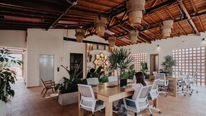 Un espacio de oficina moderno con pisos de madera, sillas de oficina blancas, una mesa de madera y lámparas de mimbre colgantes.