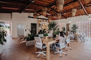 A modern office space with wooden floors, white office chairs, a wooden table, and hanging wicker lamps. - Pranik Living Co-mmunity (Medellín)