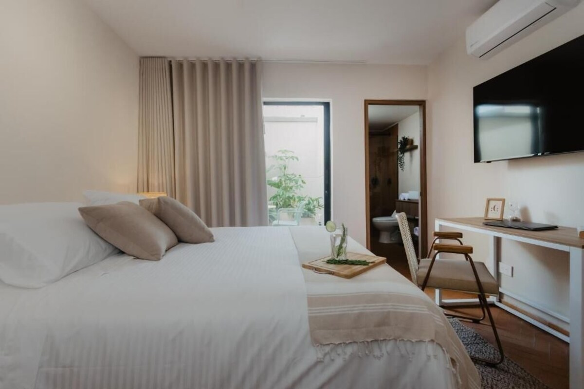 A hotel room with a bed, a desk, a chair, a TV, and a window with curtains.