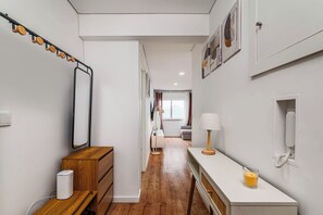 Ein Flur mit einer hölzernen Bank, einem weißen Schreibtisch, einer Lampe, einem Spiegel und einem gerahmten Bild an der Wand.