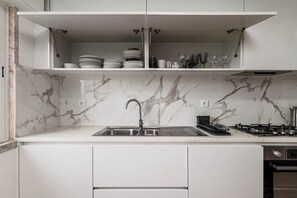 Eine Küche mit weißen Schränken, einer Marmor-Spritzschutzleiste, einem Edelstahl-Spülbecken und einem Gasherd.