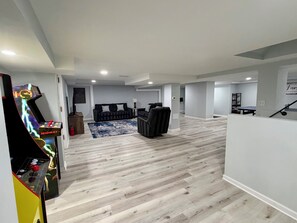 Amplia sala de estar con piso de madera, un sofá, una consola de videojuegos y una mesa de ping pong.