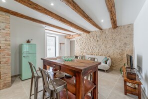 Un'area pranzo con tavolo in legno, sedie, un frigorifero verde e un muro in pietra.