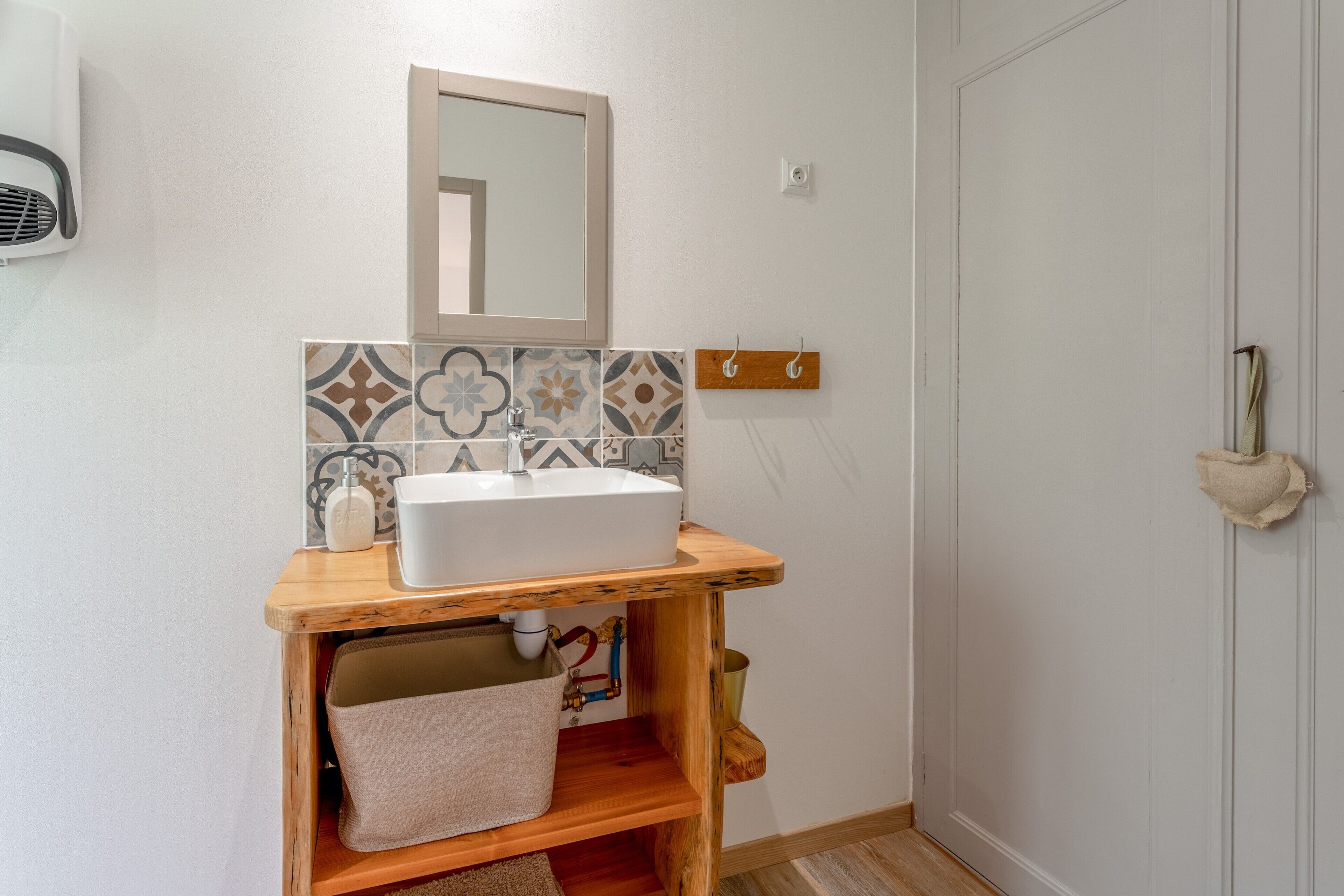 Un bagno con un mobile lavabo in legno, un lavandino bianco, uno specchio e piastrelle decorate.