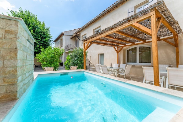 A swimming pool with a wooden pergola, outdoor seating, and a stone wall.