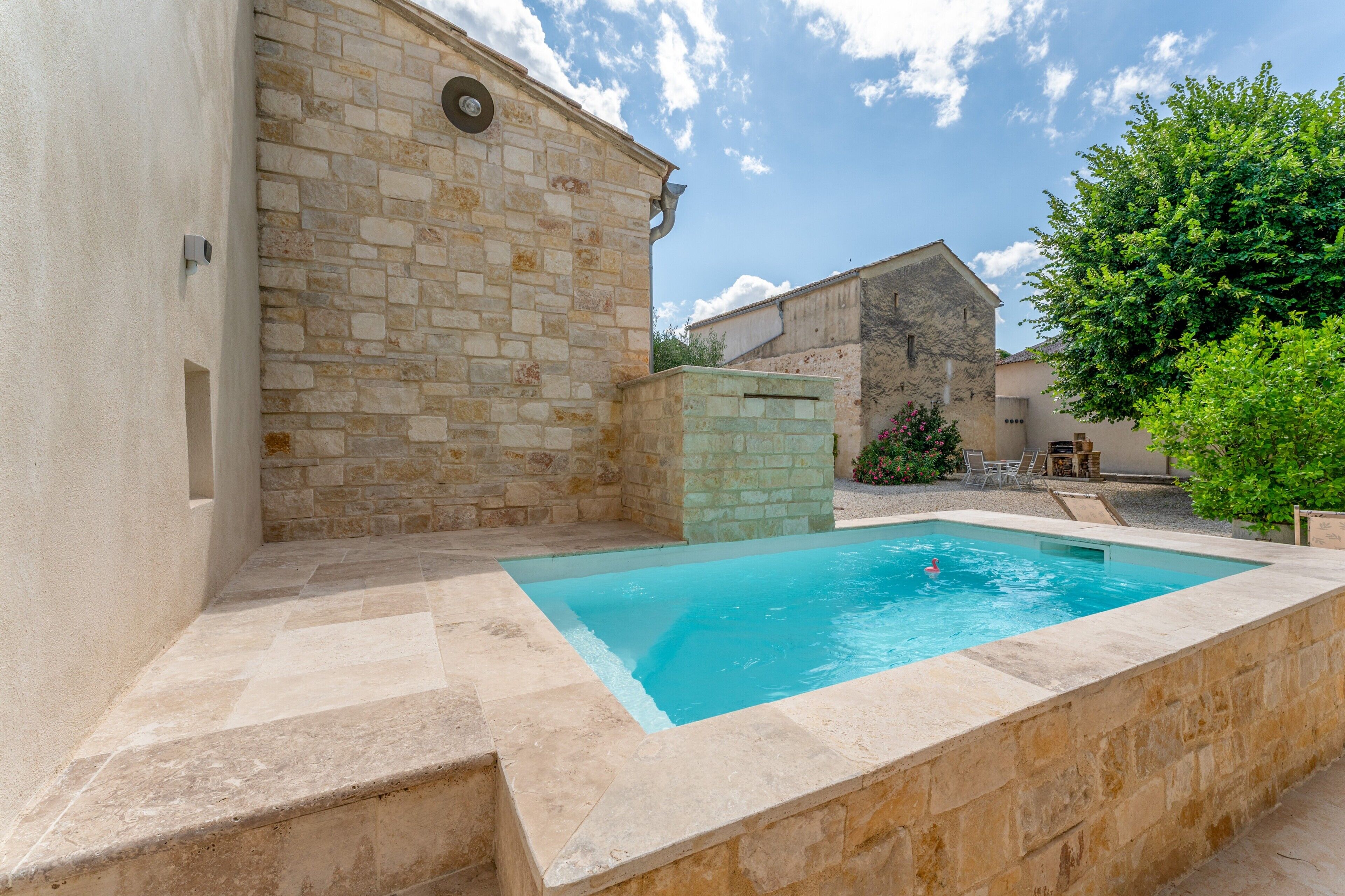 A swimming pool with stone walls, a stone building, and a tree in the background.