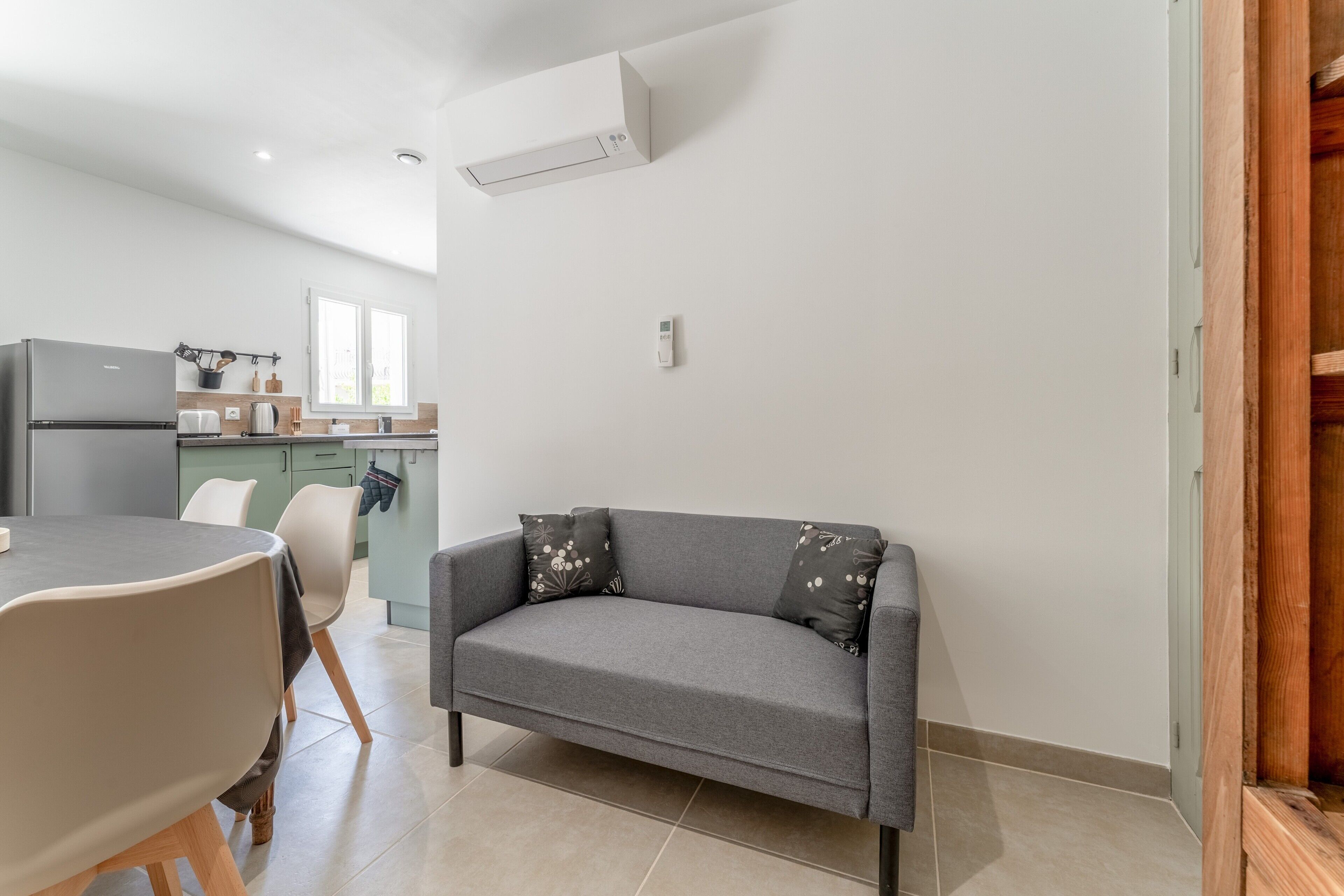 Un salon moderne avec un canapé gris, une table à manger et un coin cuisine à l’arrière-plan.