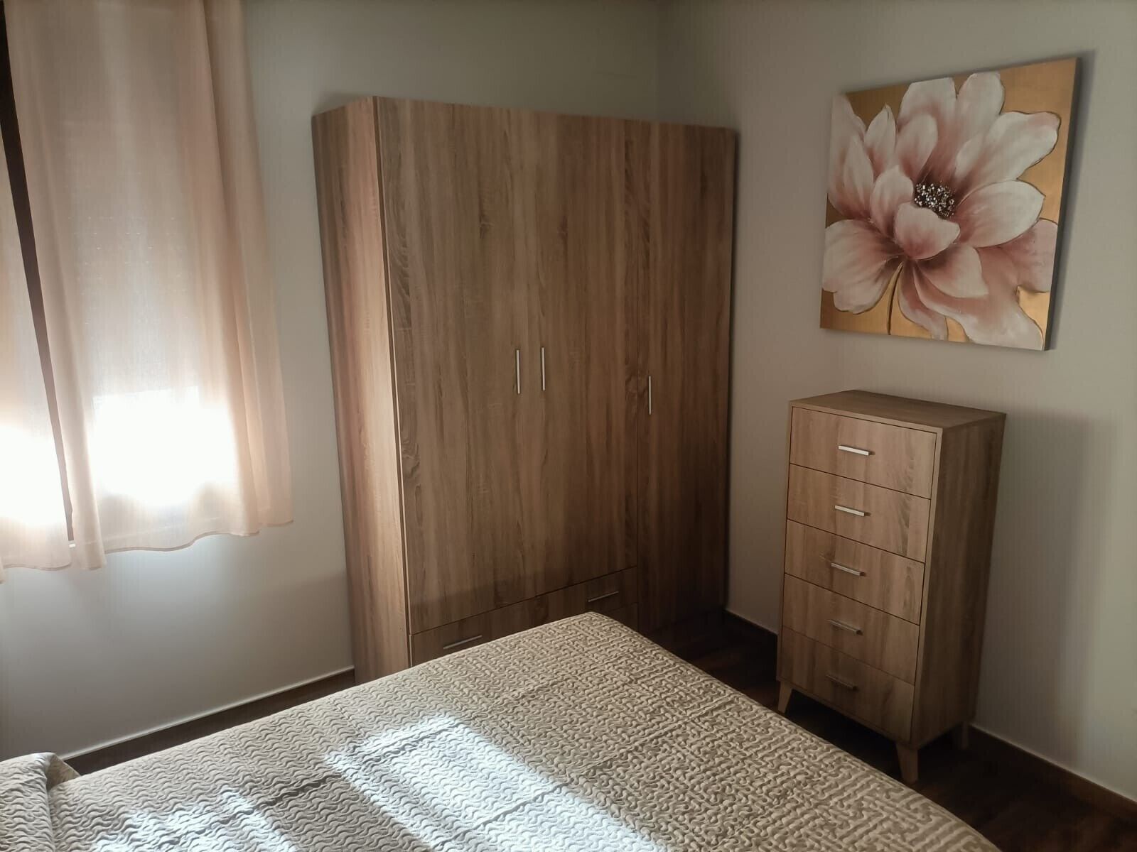 Un dormitorio con cama, armario, aparador y un cuadro en la pared.