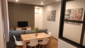 A modern living room with a sofa, a dining table with chairs, a TV, and artwork on the walls. - El Huertecillo 1 Apartment, Renaissance Village in La Mancha (Villanueva de los Infantes)