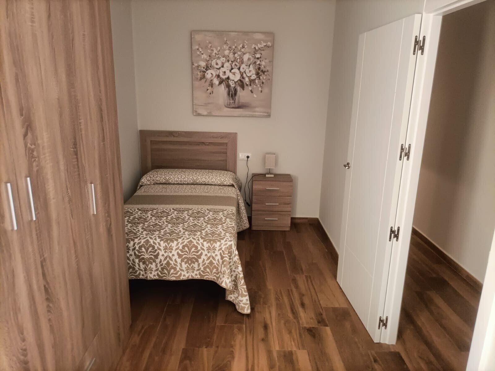 Ein Schlafzimmer mit einem hölzernen Bett, einem Nachttisch, einem Schrank und einem Bild an der Wand.