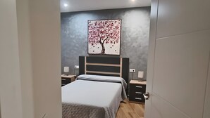 A bedroom with a bed, bedside tables, a wall-mounted painting, and a wooden floor. - El Huertecillo 1 Apartment, Renaissance Village in La Mancha (Villanueva de los Infantes)