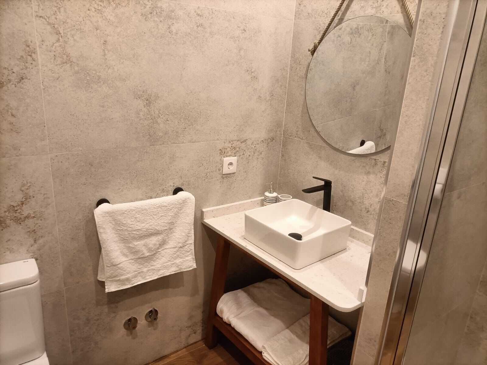 Een badkamer met een witte wastafel, een handdoekhouder, een spiegel en een douche.