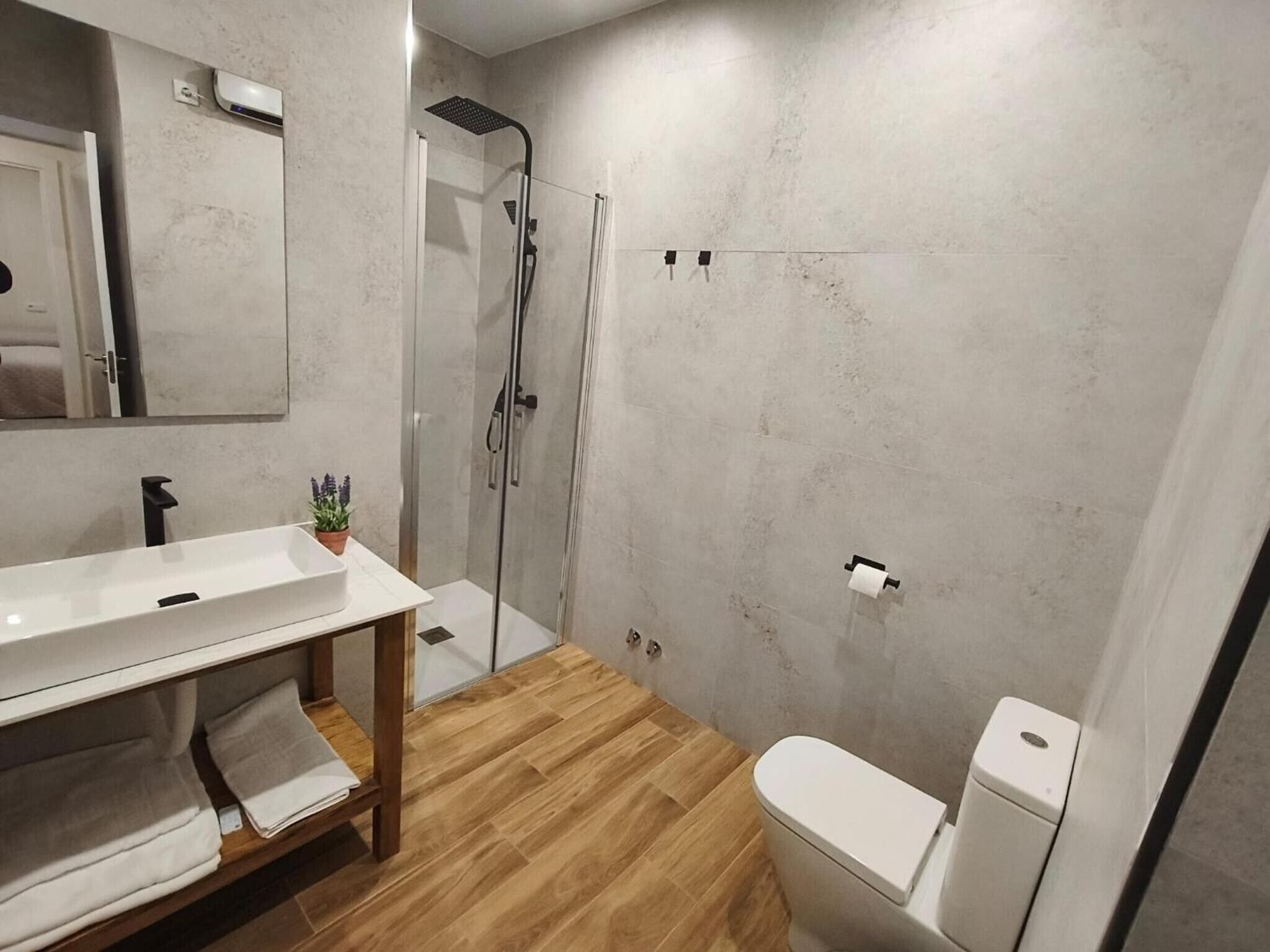 Un baño moderno con tocador de madera, ducha e inodoro.
