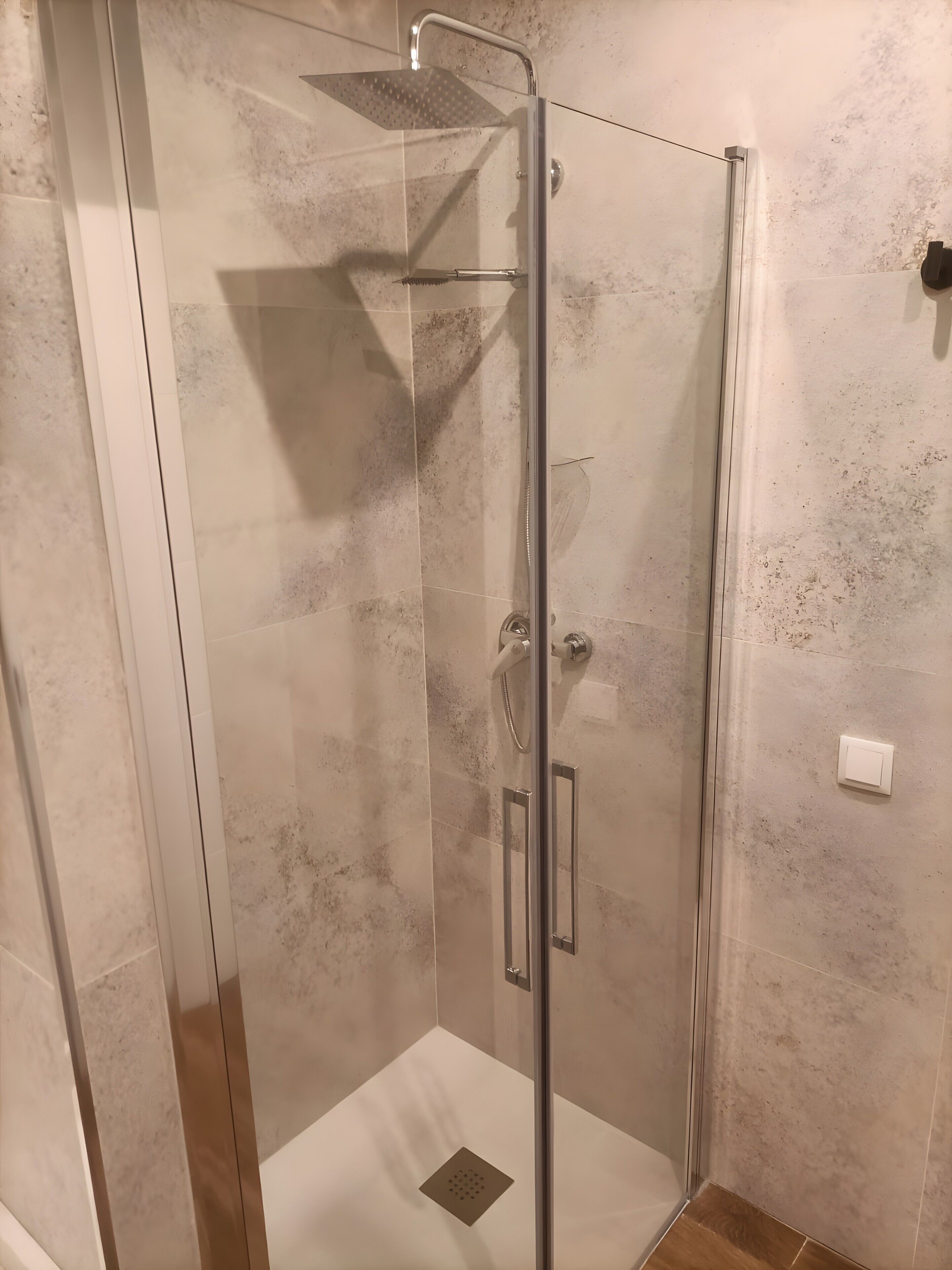 Een douchecabine met glazen wanden, een handdouche, een bedieningspaneel en een afvoer in de vloer.