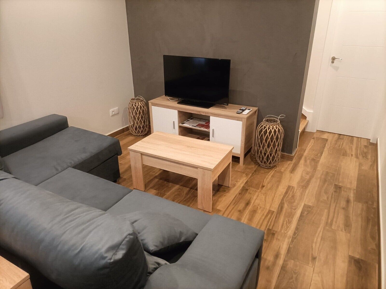 Una sala de estar con un sofá, una mesa de centro, un televisor sobre un mueble y dos jarrones decorativos.