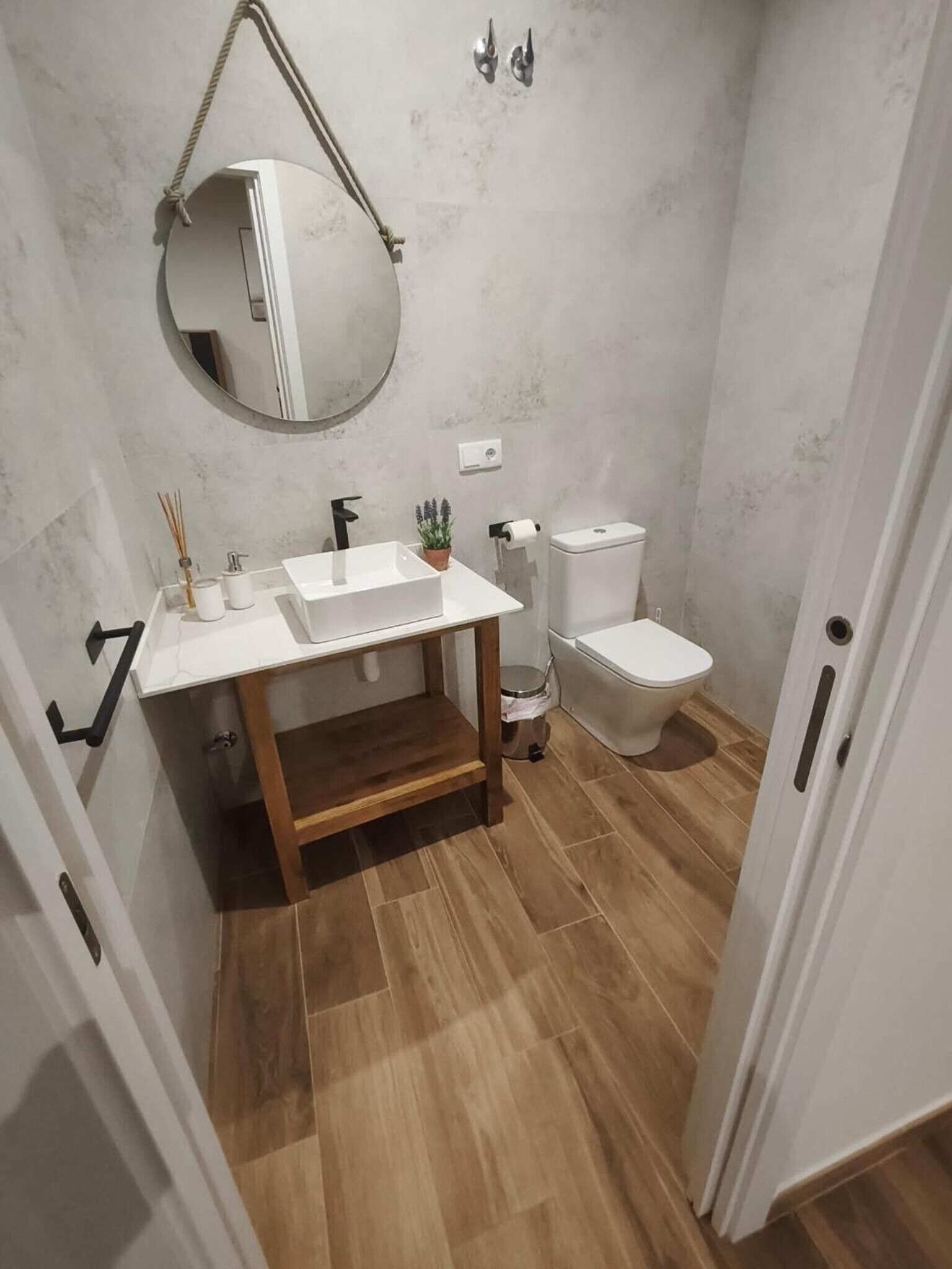 Un baño con lavamanos blanco, espejo, inodoro y suelo de madera.