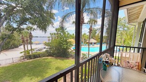 Uma varanda com vista para uma piscina, palmeiras e uma área gramada.