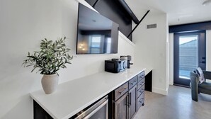 A modern kitchen with a white countertop, a potted plant, a microwave, and a large mirror. - The Lawson District | Marigold Suite (Midlothian)