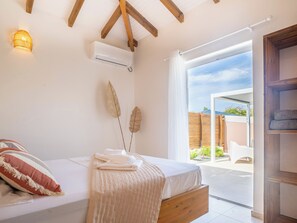 Ein Schlafzimmer mit einem Bett, einer Wandklimaanlage, einem Fenster mit Blick ins Freie und einer Holzbalkendecke.