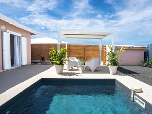 Ein Swimmingpool mit weißer Gartenmöbeln, einer Pergola und Topfpflanzen.
