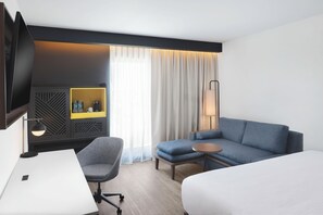 A hotel room with a bed, a desk, a chair, a sofa, a TV, a lamp, a bedside table, and a window with curtains. - Courtyard by Marriott Torreon (Torreon)