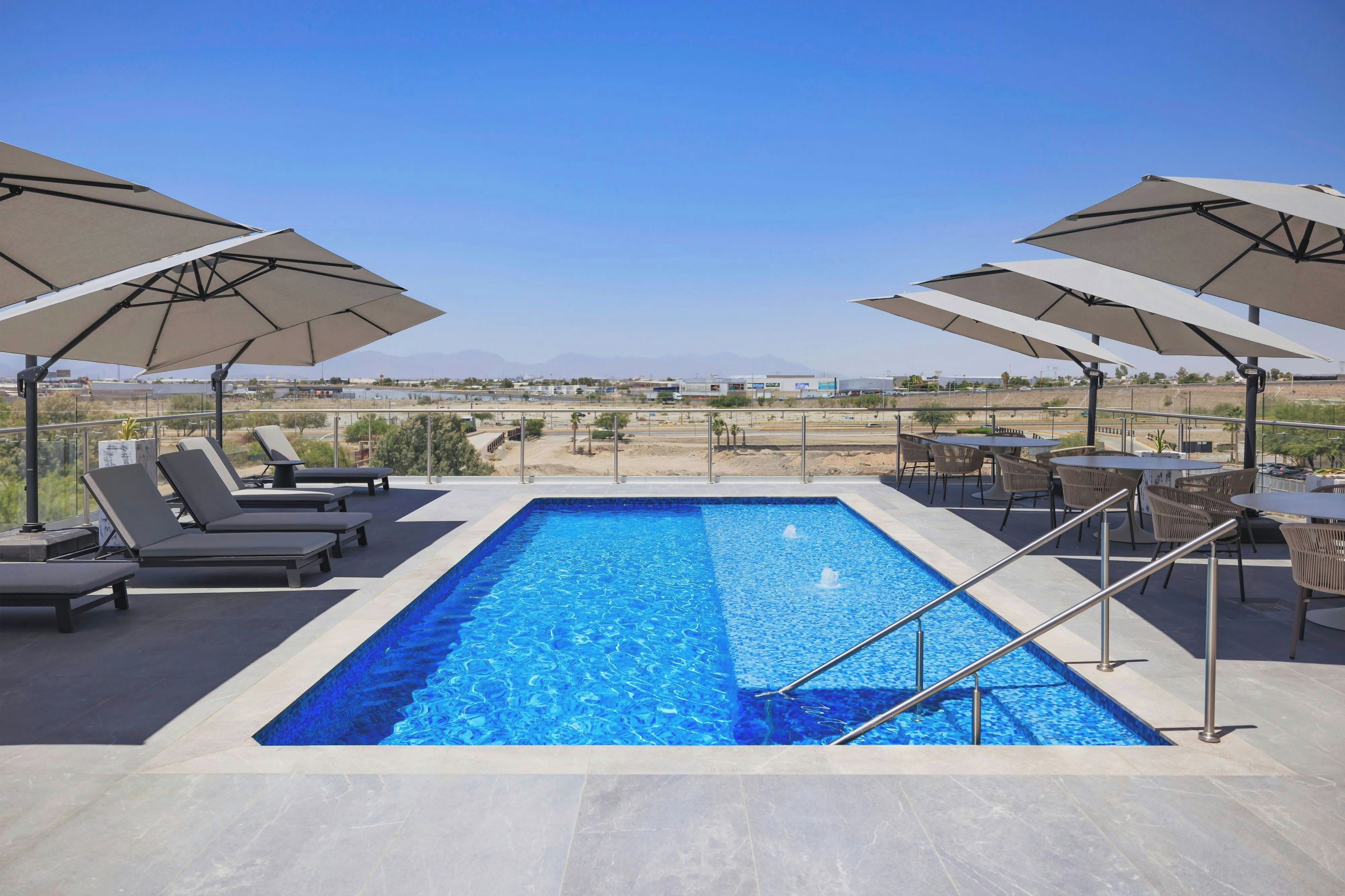 A rectangular swimming pool with a clear blue water surface, surrounded by lounge chairs and umbrellas.