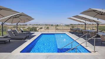 A rectangular swimming pool with a clear blue water surface, surrounded by lounge chairs and umbrellas.