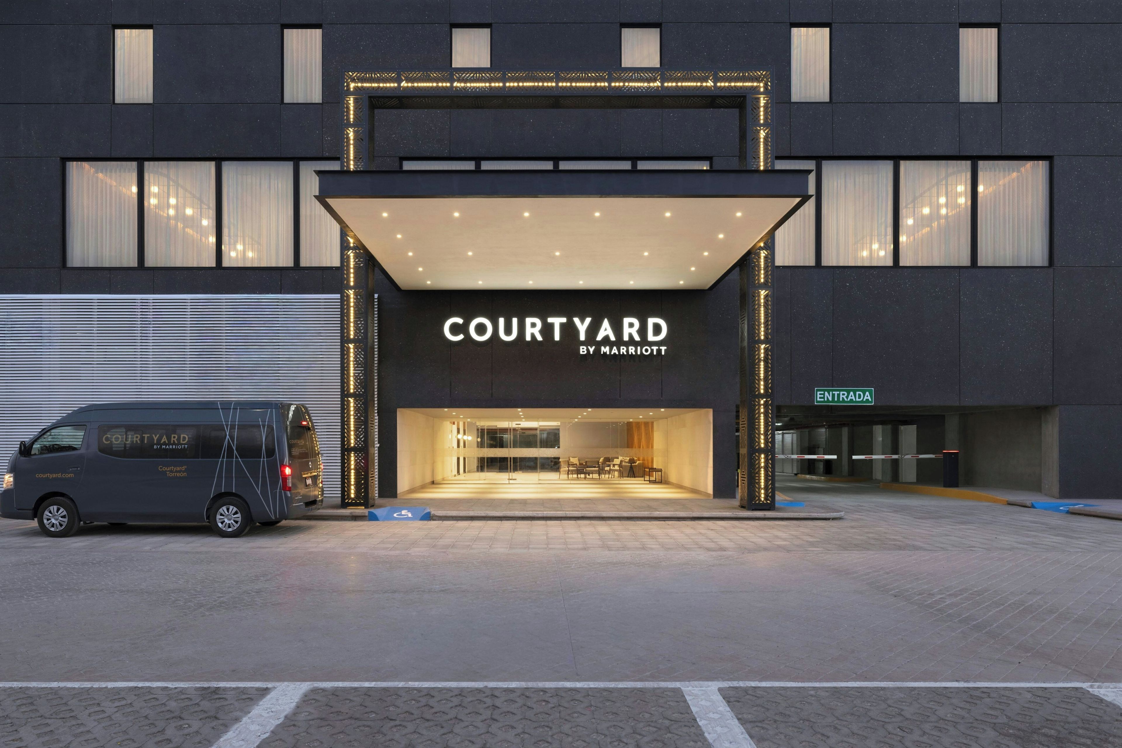 Un edificio moderno con un letrero que dice 'COURTYARD BY MARRIOTT' y una furgoneta estacionada adelante.