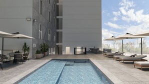 A modern outdoor pool area with lounge chairs and umbrellas, surrounded by a building with large windows. - Courtyard by Marriott Torreon (Torreon)