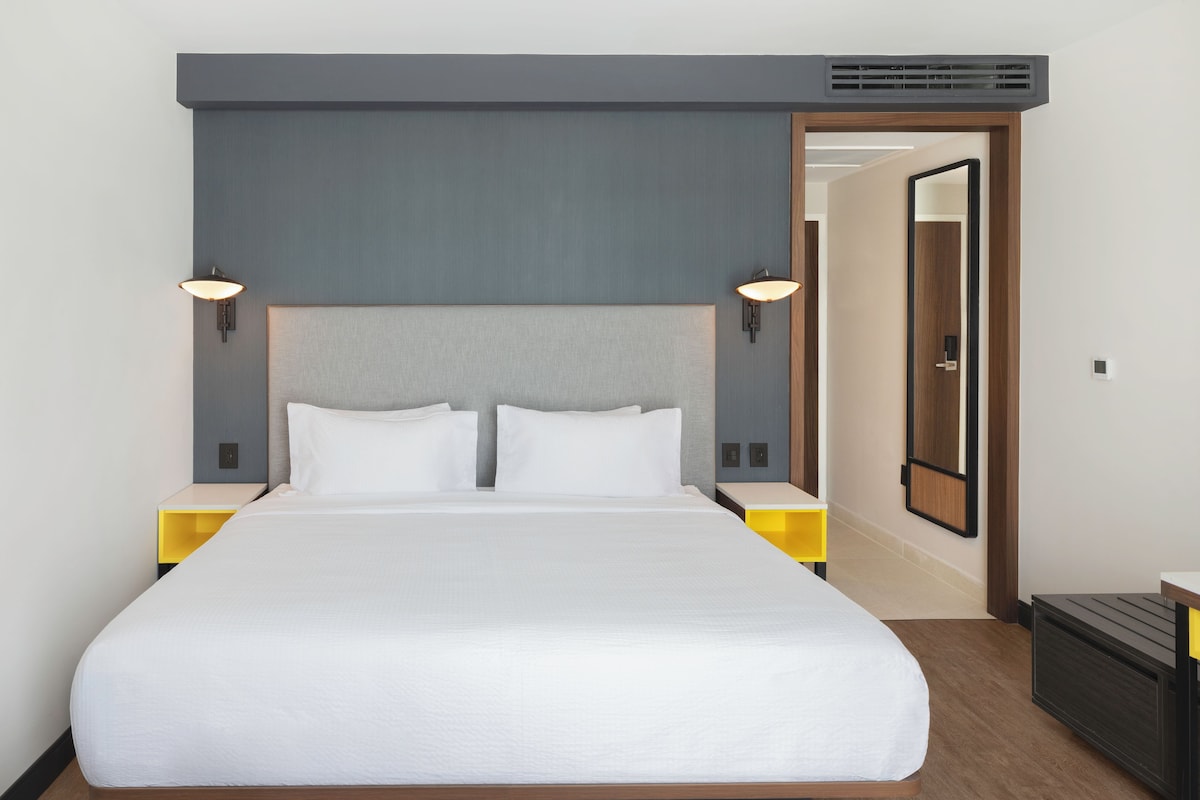 Une chambre d’hôtel avec un grand lit, deux tables de chevet, une tête de lit et une porte donnant sur une autre pièce.