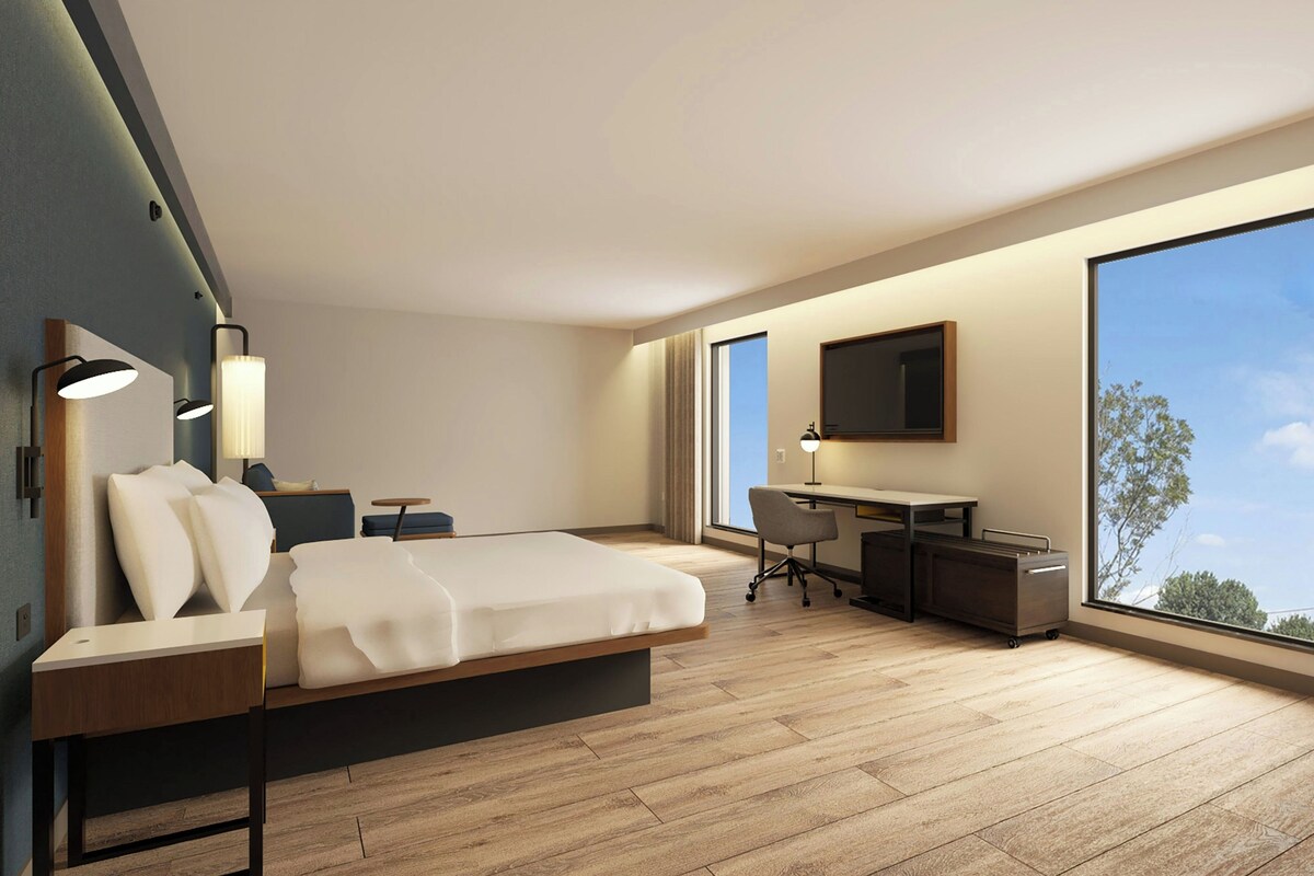 Una habitación de hotel moderna con cama, escritorio y ventana grande.